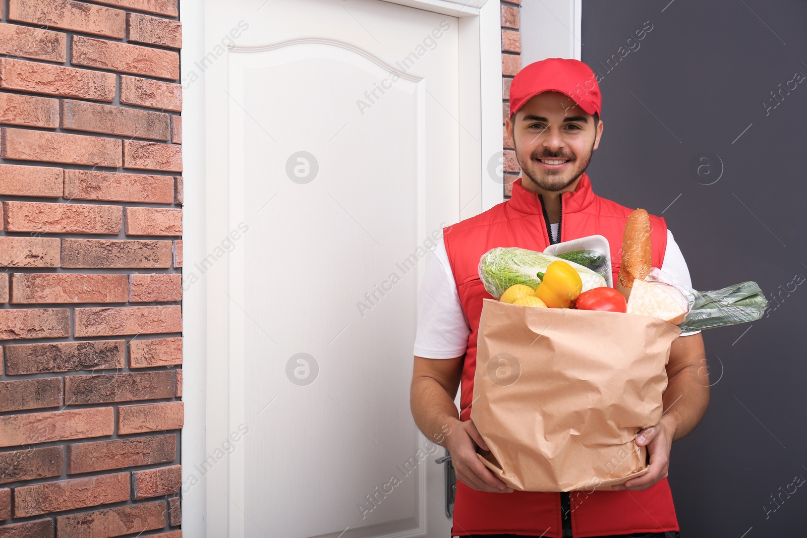 Photo of Food delivery courier holding paper bag with products indoors. Space for text