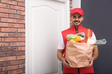 Photo of Food delivery courier holding paper bag with products indoors. Space for text