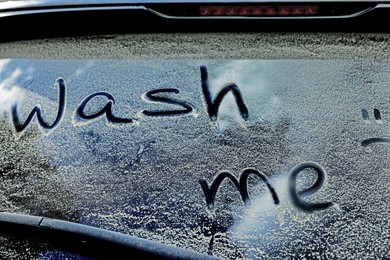 Photo of Phrase Wash me written on dirty car window outdoors, closeup