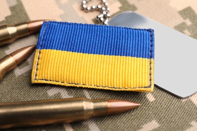 Photo of Ukrainian army patch, bullets and ID tags on military camouflage, closeup