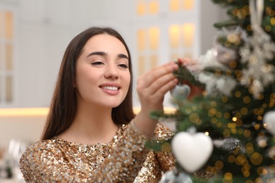 Photo of Smiling woman decorating Christmas tree with baubles in kitchen