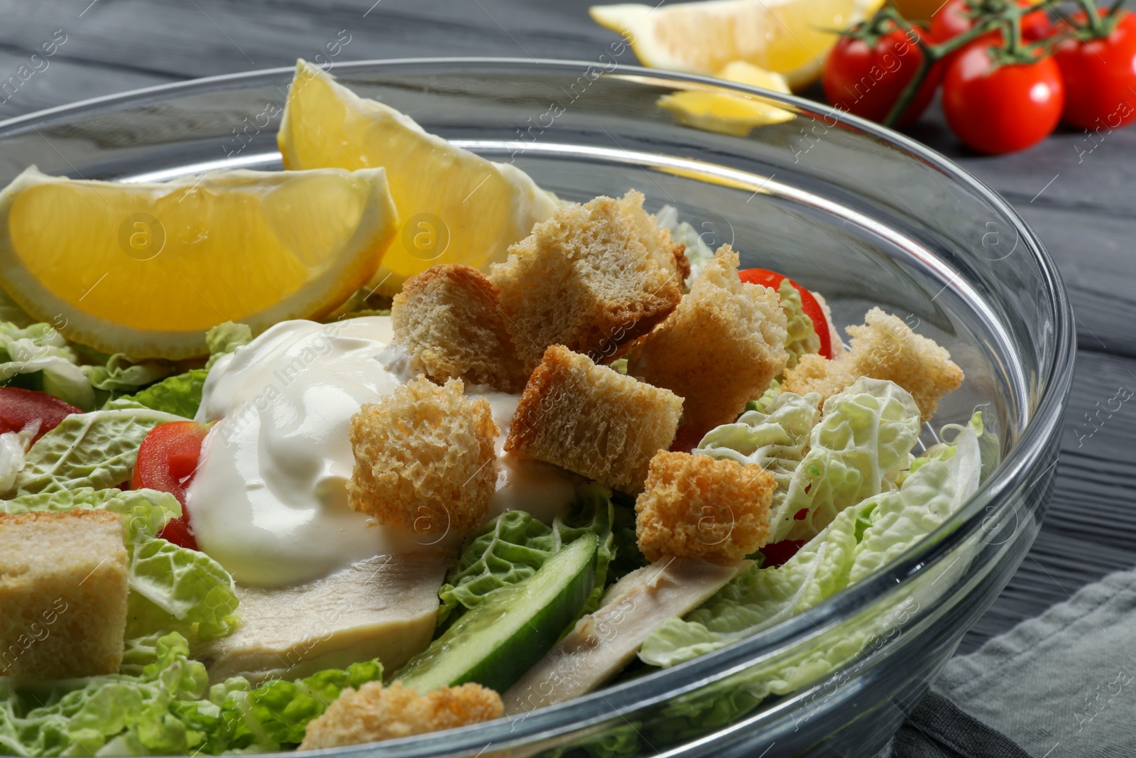 Photo of Bowl of delicious salad with Chinese cabbage, lemon, tomatoes and bread croutons on black wooden table, closeup