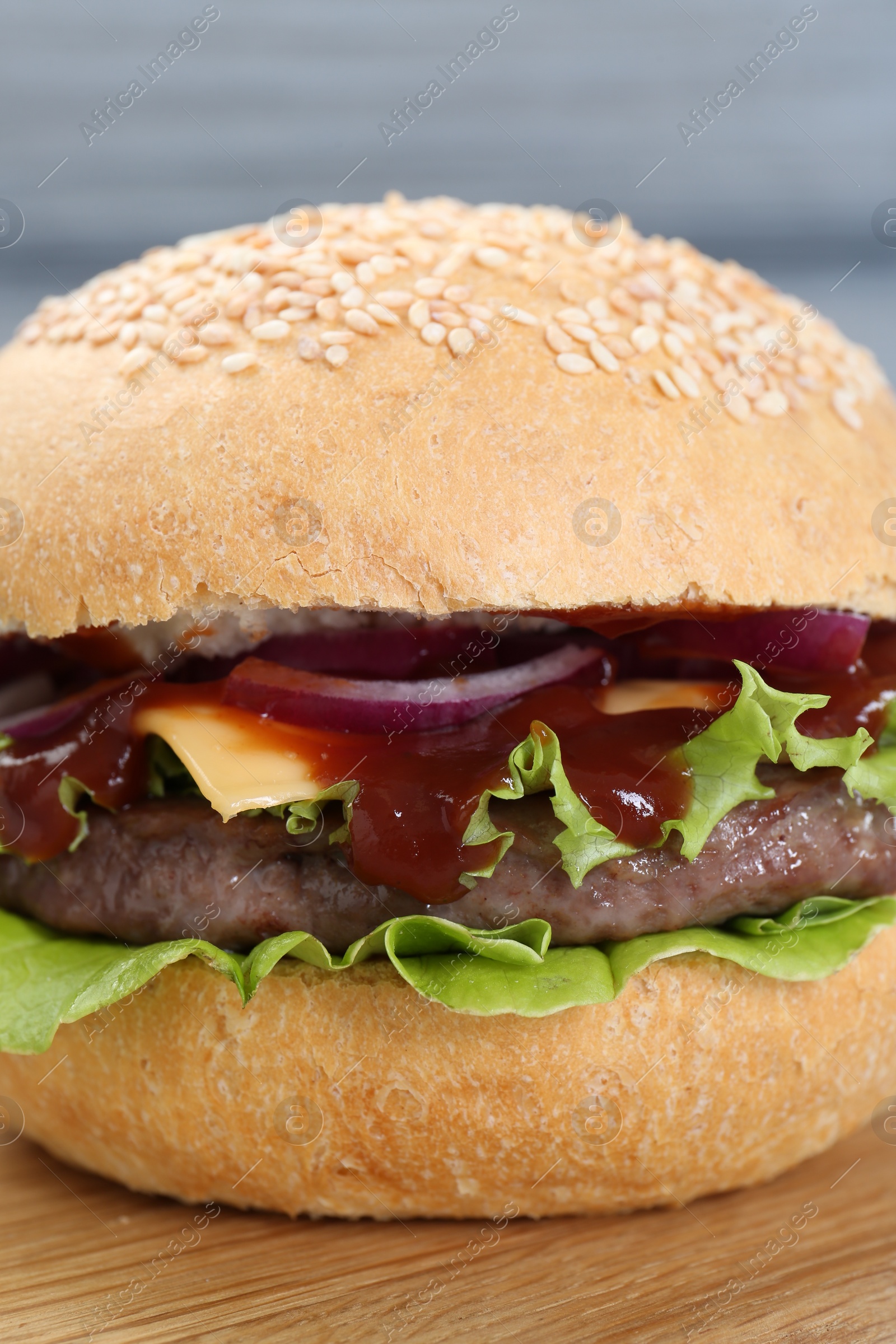 Photo of Delicious cheeseburger with lettuce, onion, ketchup and patty on table, closeup