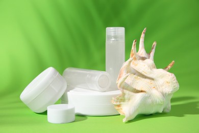 Photo of Jars of cream, shampoo samples, lip balm and seashell on light green background
