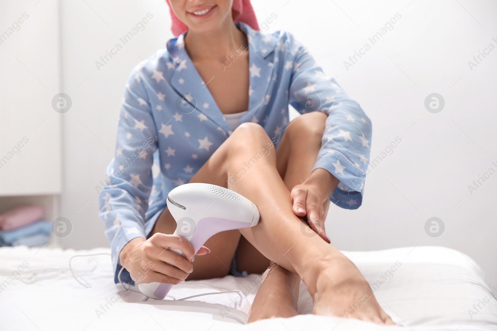 Photo of Young woman epilating her legs in bedroom, closeup