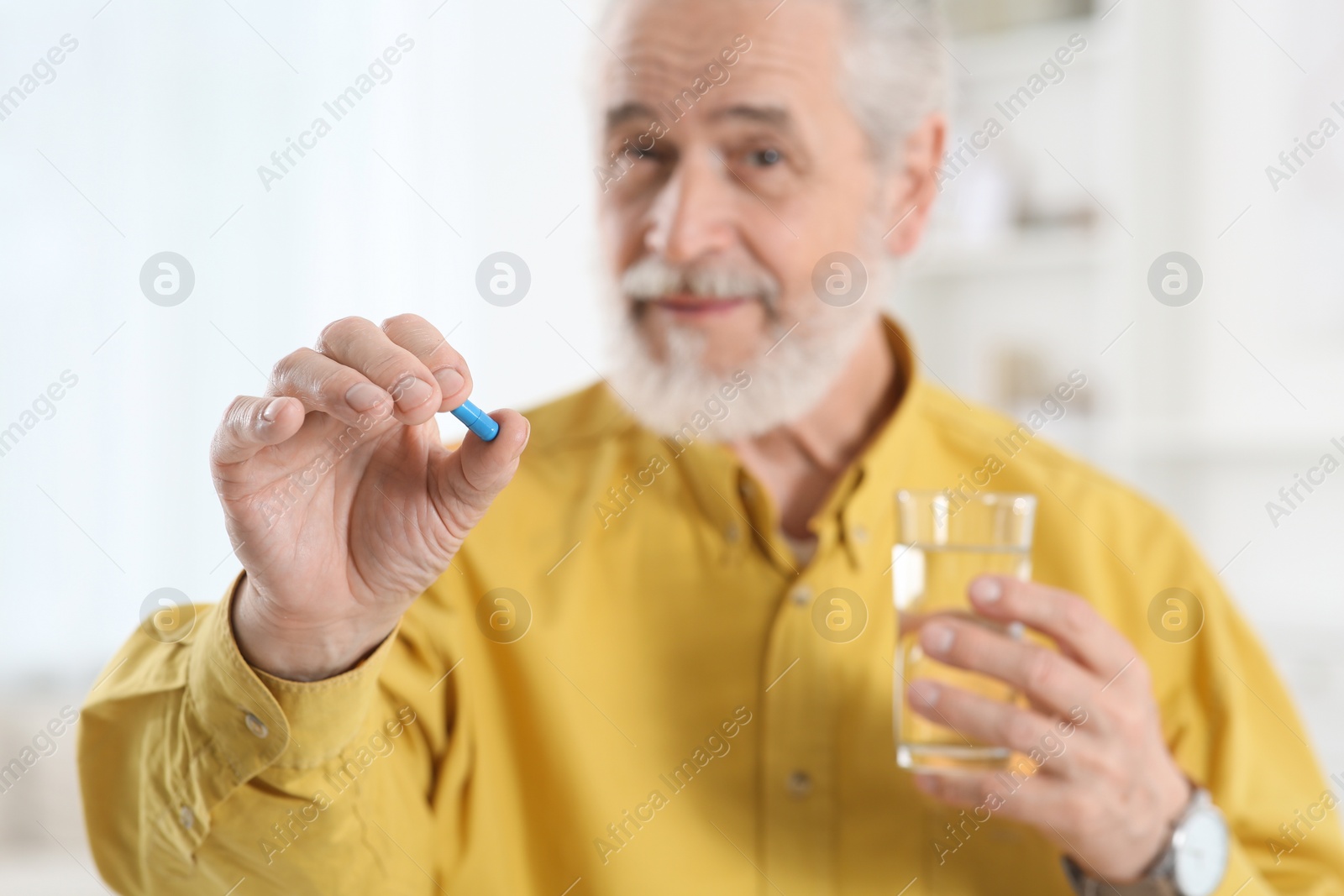 Photo of Senior man with glass of water and pill indoors, selective focus
