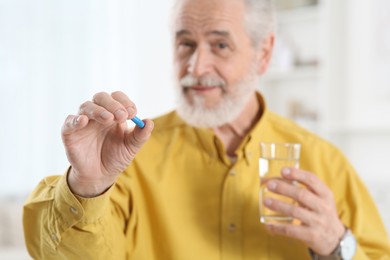 Senior man with glass of water and pill indoors, selective focus