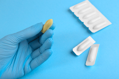 Photo of Woman holding suppository on light blue background, closeup. Hemorrhoid treatment