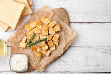 Delicious crispy croutons with rosemary and sauce on white wooden table, flat lay, Space for text