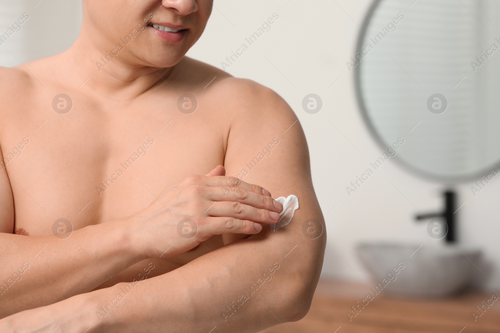 Photo of Man applying body cream onto his arm indoors, closeup. Space for text