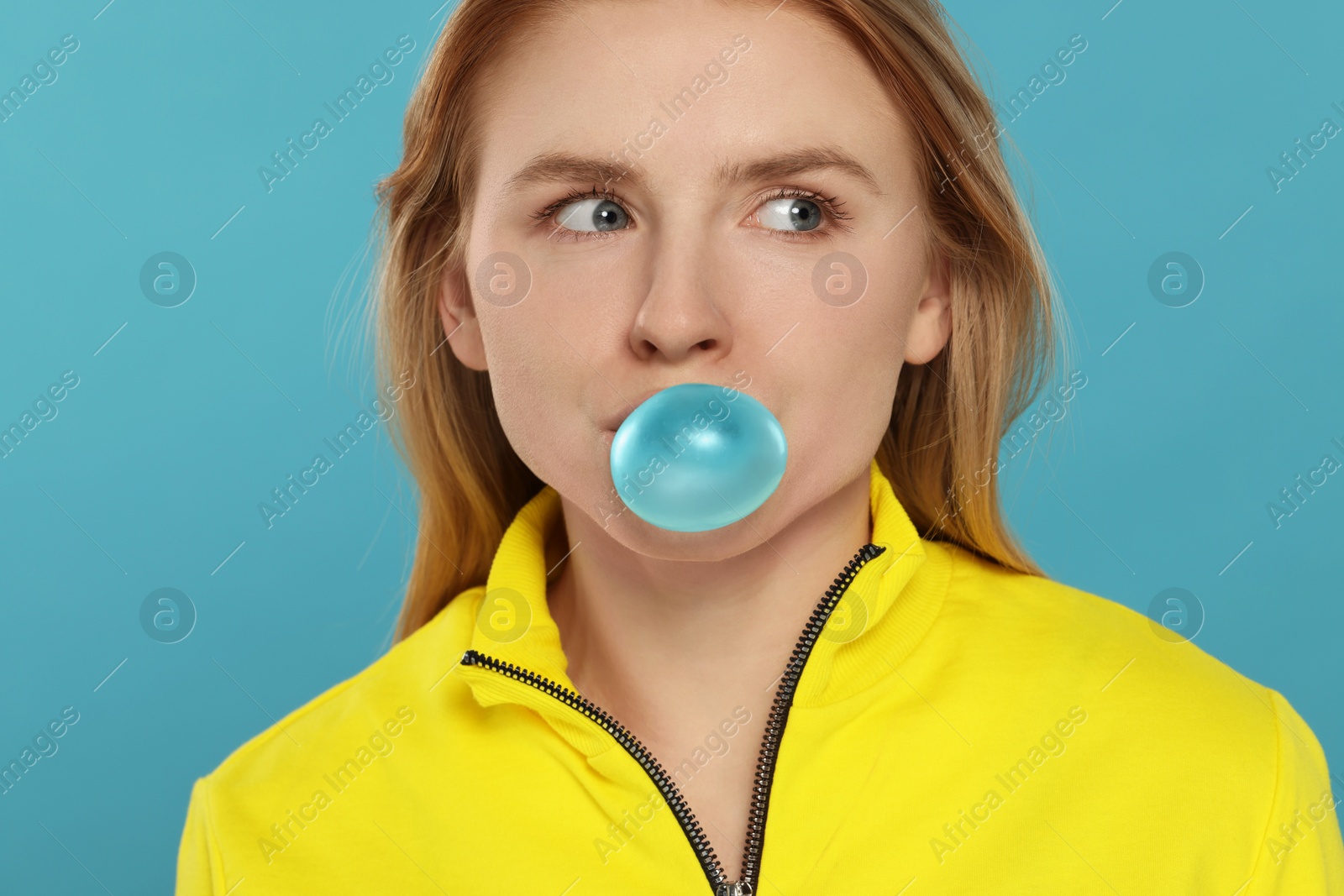 Photo of Beautiful young woman blowing bubble gum on light blue background