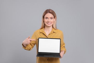 Happy woman showing laptop on light grey background