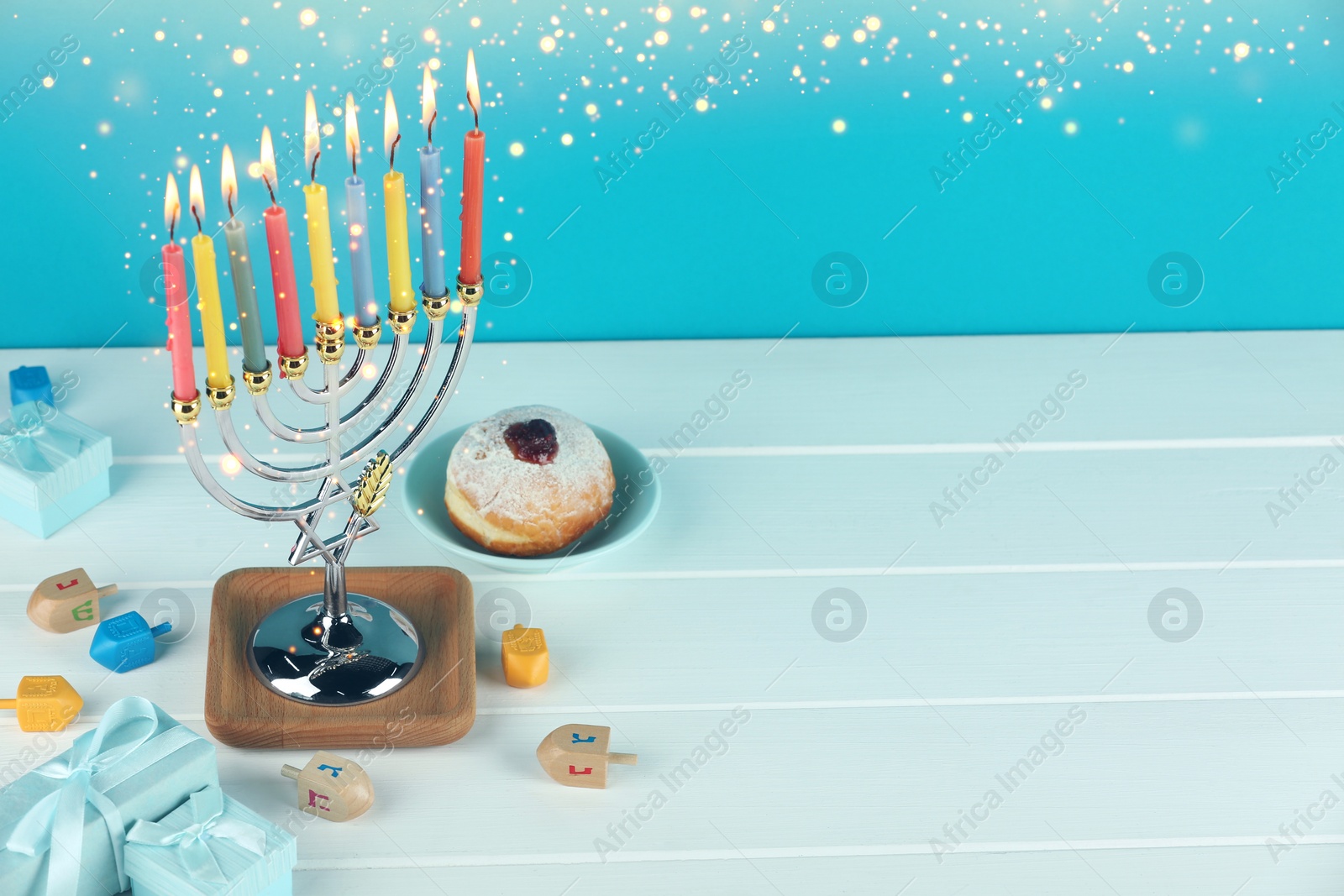 Image of Hanukkah celebration. Menorah with burning candles, dreidels, gift boxes and donut on white wooden table, space for text
