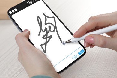 Electronic signature. Woman using stylus and mobile phone at white table, closeup