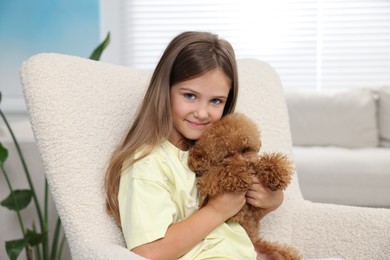 Little child with cute puppy in armchair at home. Lovely pet