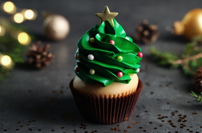 Photo of Cupcake decorated with creamy Christmas tree on dark table, closeup