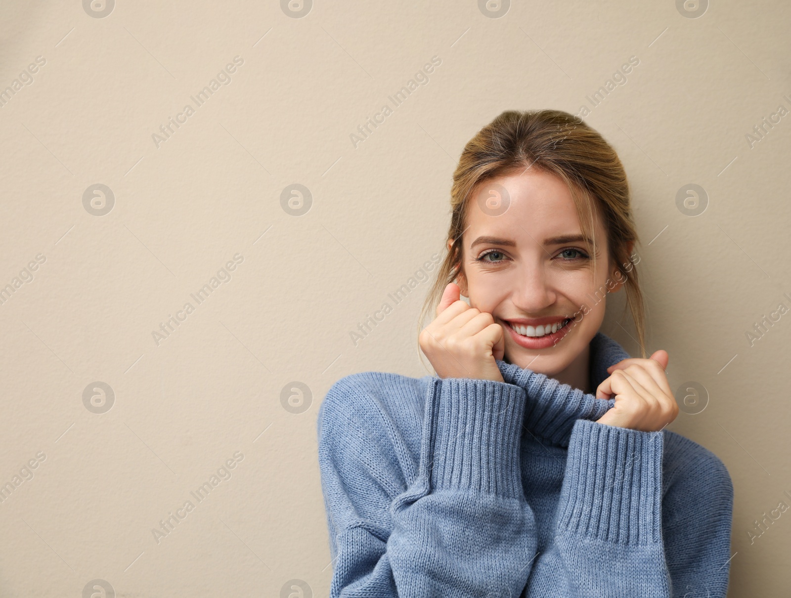 Photo of Beautiful young woman wearing knitted sweater on beige background. Space for text