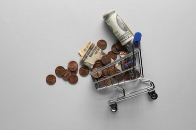 Photo of Small metal shopping cart with coins and dollar banknotes on light background, flat lay