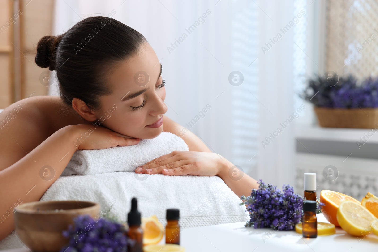 Photo of Beautiful young woman relaxing on massage couch and bottles of essential oil with ingredients on table in spa salon