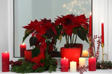 Photo of Potted poinsettias, burning candles and festive decor on windowsill in room. Christmas traditional flower