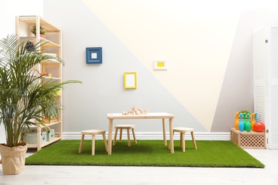 Photo of Stylish playroom interior with table, stools and green carpet