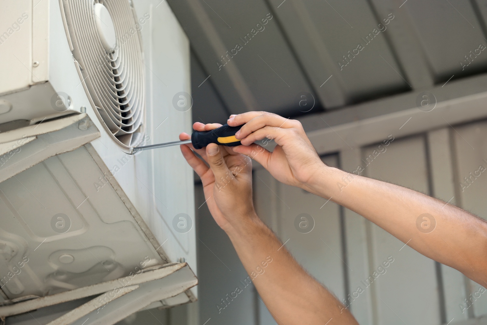 Photo of Professional technician maintaining modern air conditioner outdoors, closeup