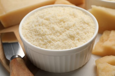 Photo of Bowl with grated parmesan cheese on white table, closeup