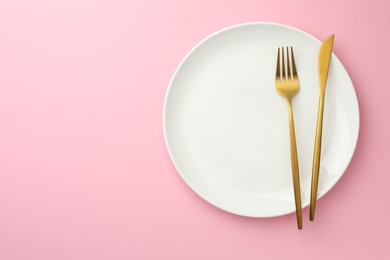 Plate, fork and knife on pink background, top view. Space for text