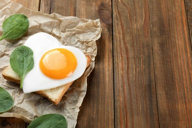 Tasty toast with heart shaped fried egg and spinach on wooden table, space for text