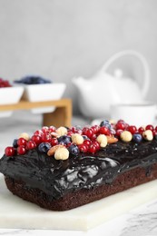 Delicious chocolate sponge cake with berries and nuts on white table, closeup