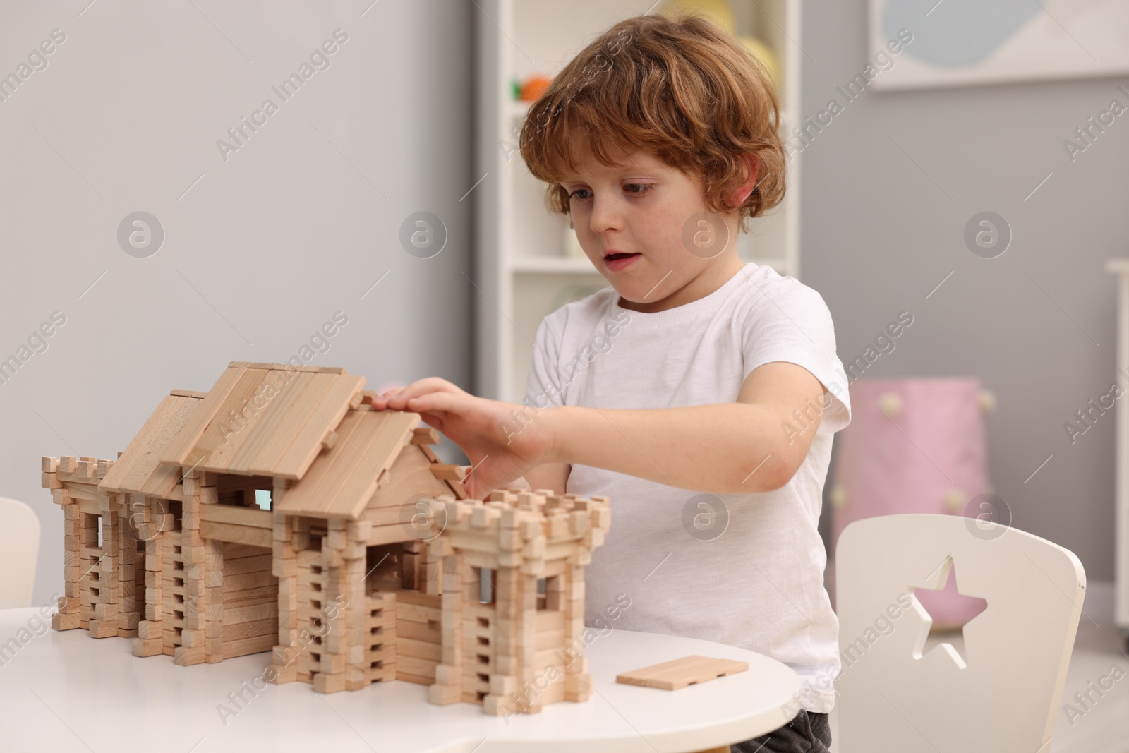 Photo of Little boy playing with wooden entry gate at table in room. Child's toy