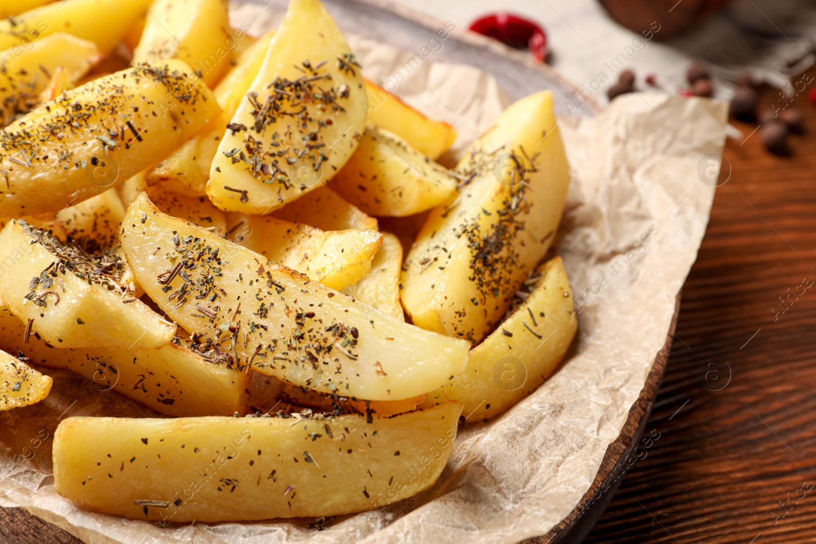 Photo of Board with tasty baked potato wedges and spices on wooden table, closeup