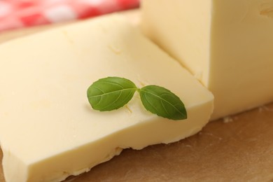 Block of tasty butter with basil on table, closeup