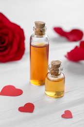 Bottles of love potion and paper hearts on white wooden table, closeup