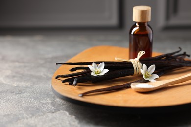 Photo of Bunch of vanilla pods, flowers, sugar and bottle with essential oil on grey textured table, closeup. Space for text