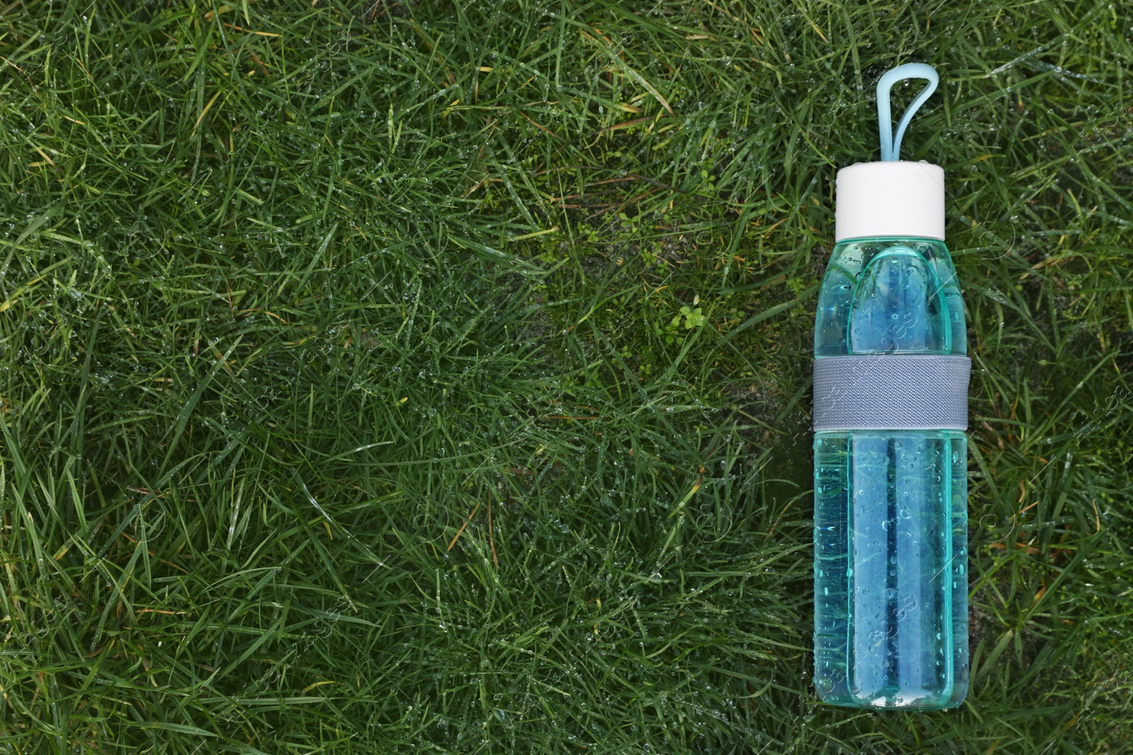 Photo of Glass bottle of fresh water on green grass outdoors, top view. Space for text