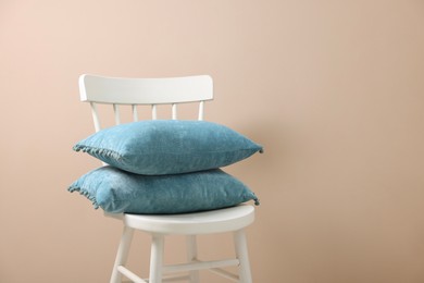 Photo of Stack of soft pillows on chair near beige wall. Space for text