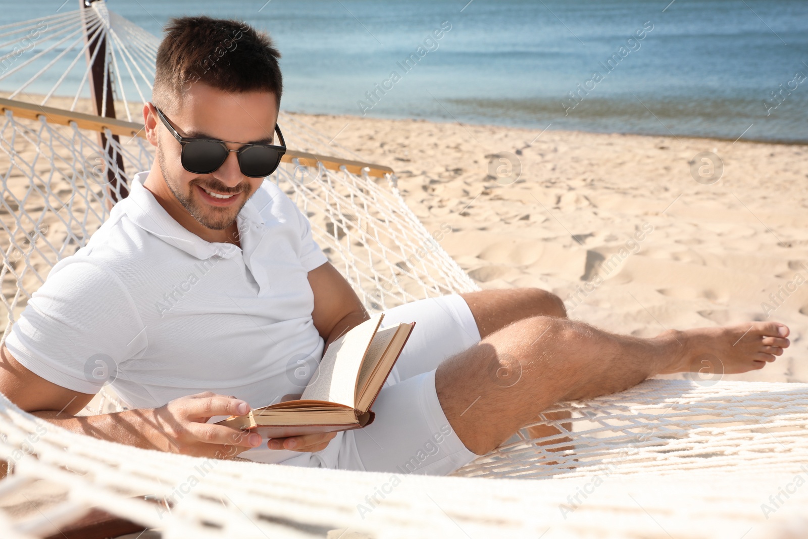 Photo of Young man reading book in hammock on beach