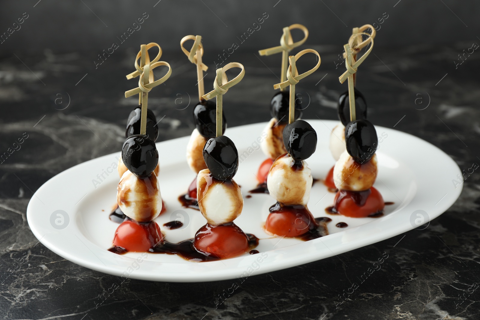 Photo of Tasty canapes with black olives, mozzarella and cherry tomatoes on dark textured table, closeup