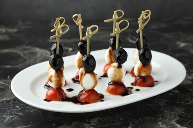 Photo of Tasty canapes with black olives, mozzarella and cherry tomatoes on dark textured table, closeup