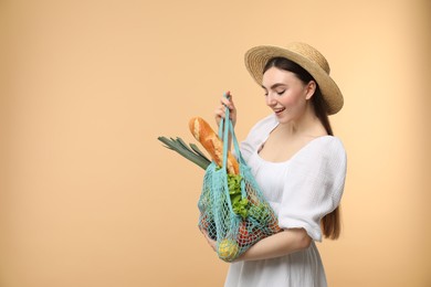 Photo of Woman with string bag of fresh vegetables and baguette on beige background, space for text