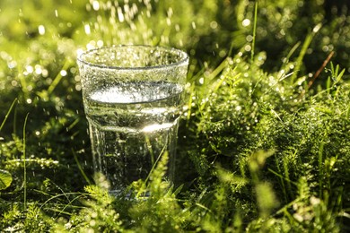 Glass of fresh water on green grass outdoors, closeup