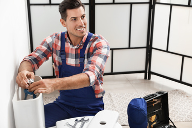 Professional plumber working with toilet bowl in bathroom