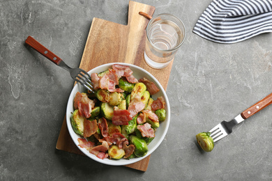 Photo of Delicious roasted Brussels sprouts with bacon served on grey table, flat lay