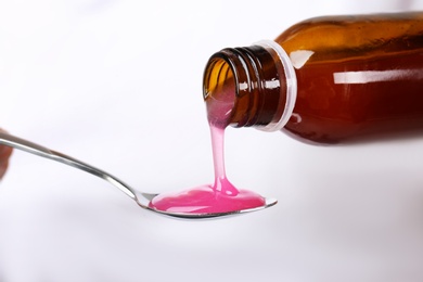 Photo of Pouring cough syrup into spoon on white background, closeup
