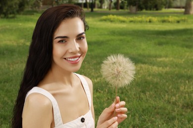 Beautiful young woman with large dandelion in park, space for text. Allergy free concept
