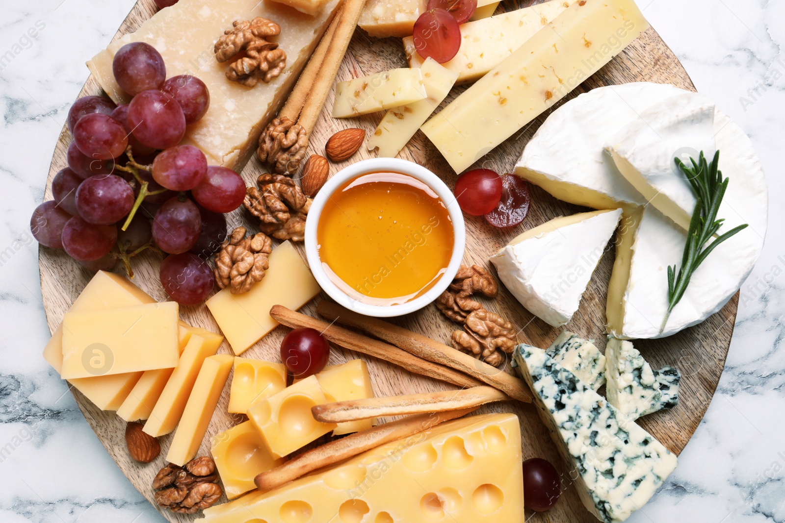 Photo of Cheese plate with honey, grapes and nuts on white marble table, top view