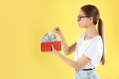 Photo of Young woman with wallet full of money on yellow background