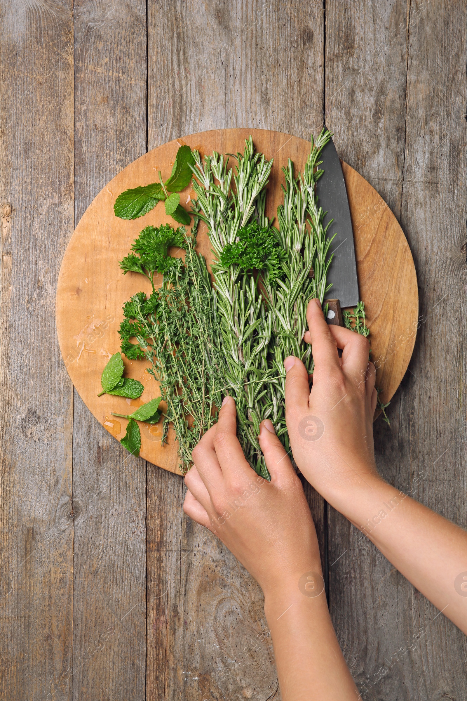 Photo of Woman with rosemary and other herbs on wooden background, top view