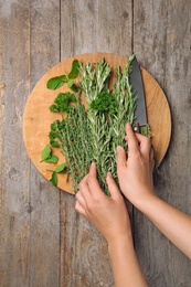 Woman with rosemary and other herbs on wooden background, top view